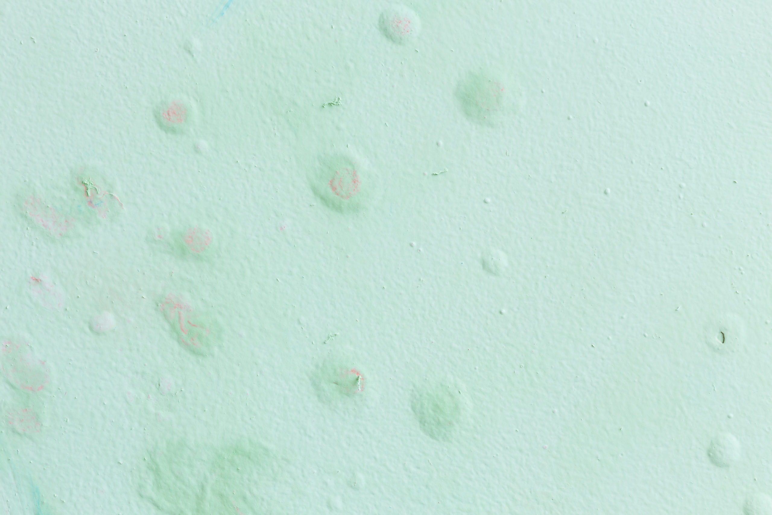 Parede verde-clara com textura irregular, pequenas bolhas, descascados e manchas suaves em tons de rosa e azul