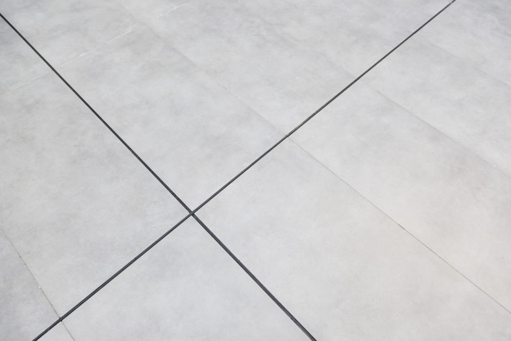 Piso de porcelanato cinza claro com rejuntes escuros formando linhas diagonais e um padrão geométrico abstrato.