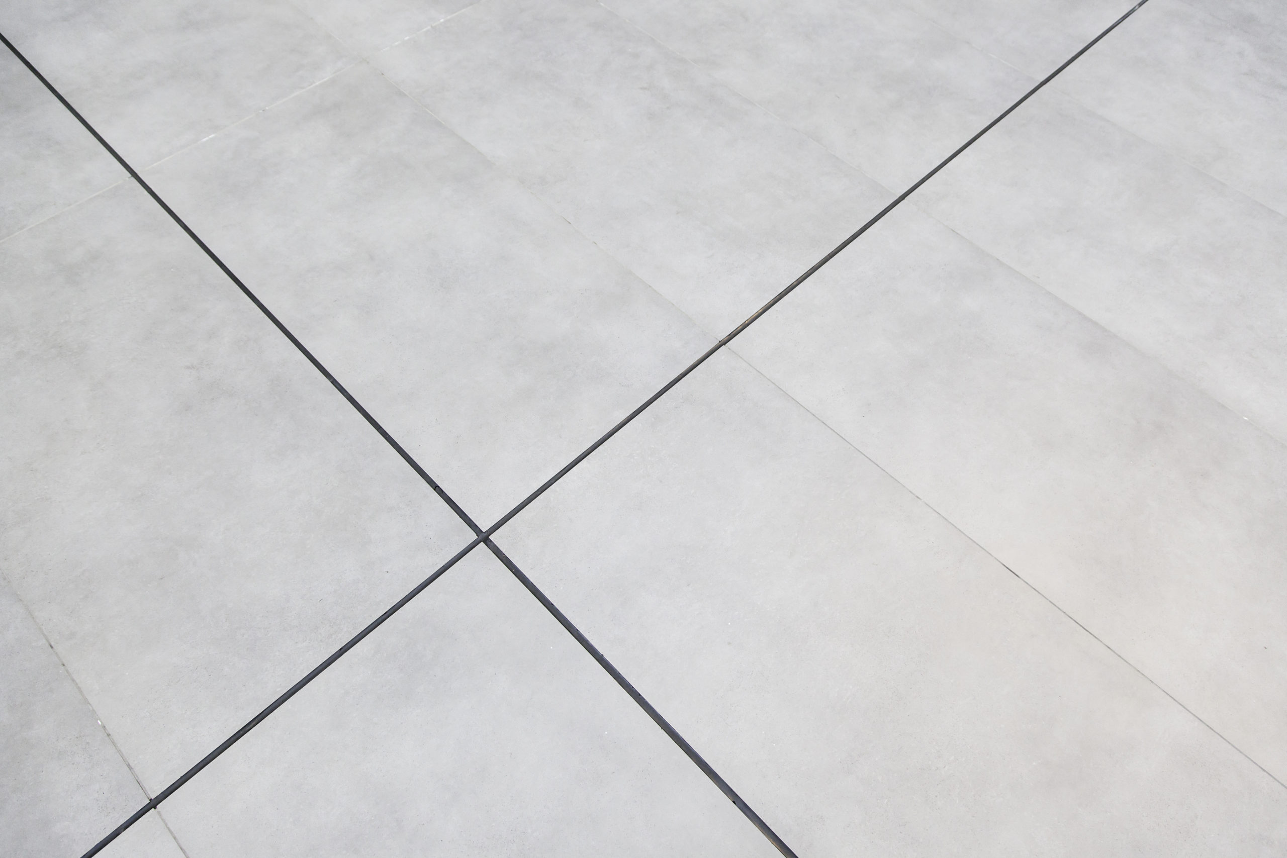 Piso de porcelanato cinza claro com rejuntes escuros formando linhas diagonais e um padrão geométrico abstrato.