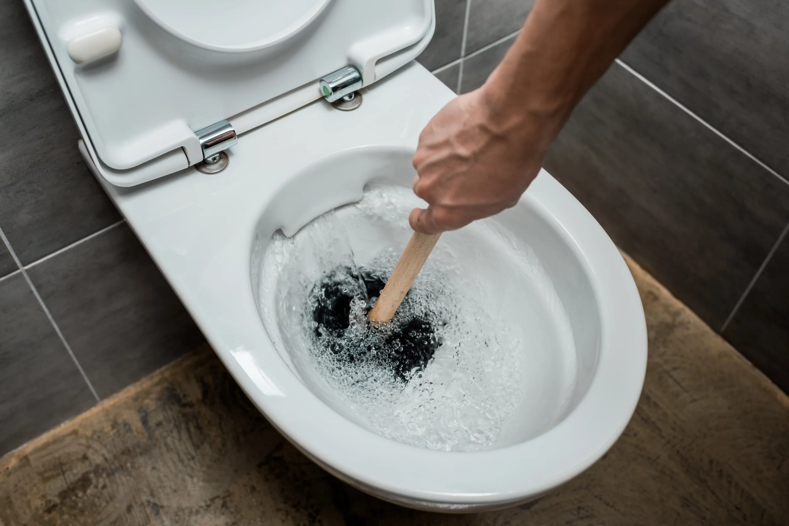 Pessoa desentupindo um vaso sanitário com um desentupidor enquanto a água circula no interior.