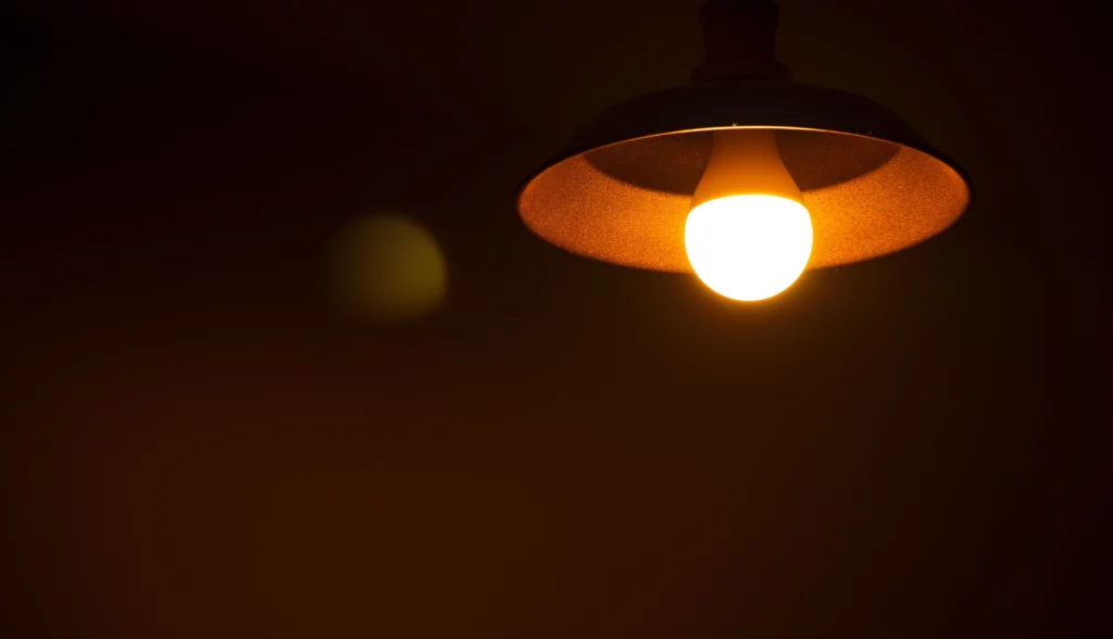 Lâmpada acesa pendurada em um ambiente escuro, emitindo luz quente e criando uma atmosfera intimista.