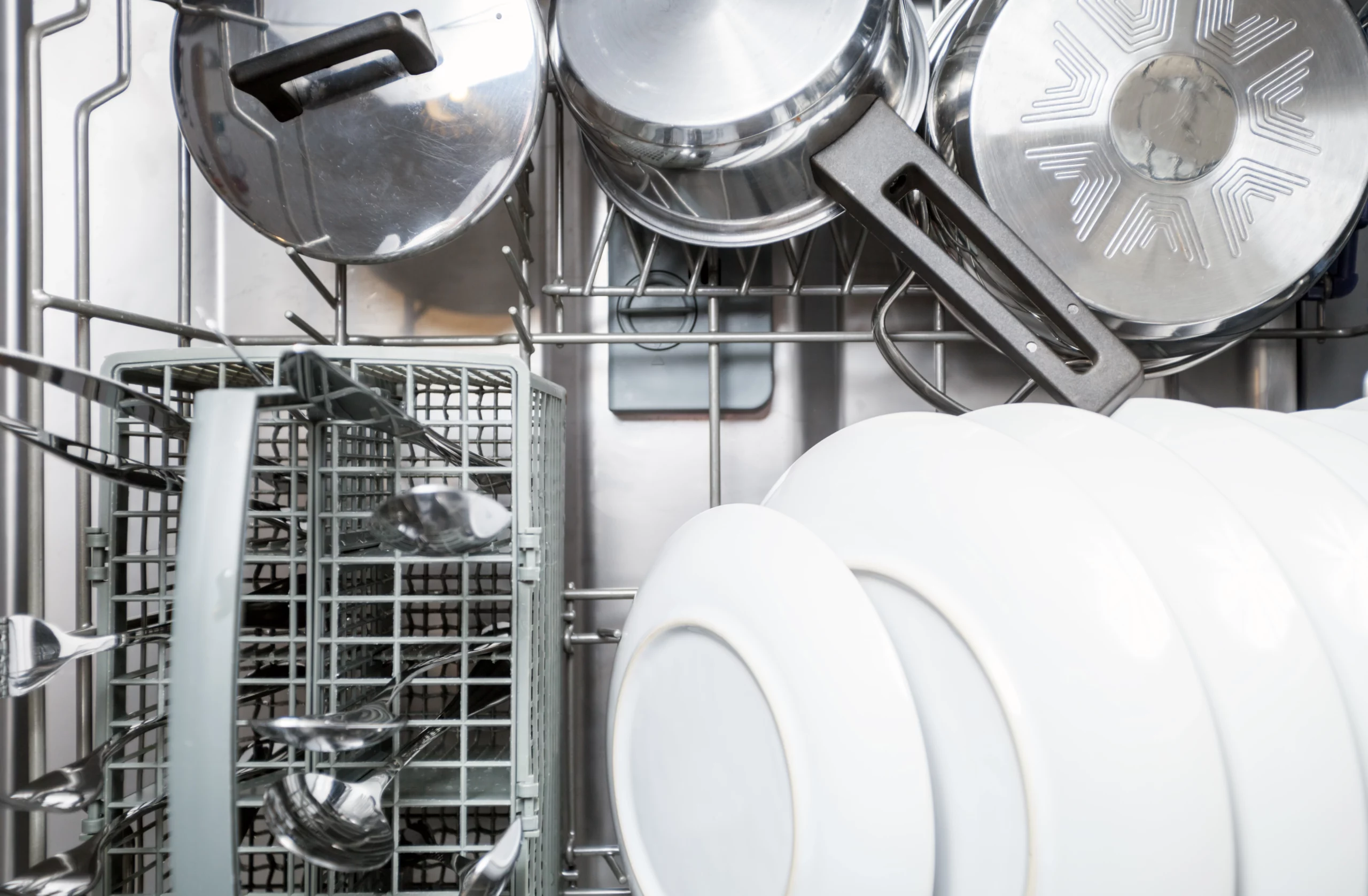 Interior de uma lava-louças aberta com panelas de inox, pratos brancos, talheres organizados no cesto e utensílios acomodados corretamente para o ciclo de lavagem.